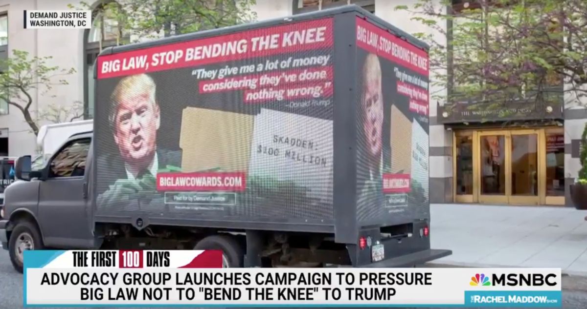 Image of a shot from a video clip on The Rachel Maddow Show at MSNBC. The chyron at the bottom reads "Advocacy group launches campaign to pressure big law not to "bend the knee" to Trump". The shot is of a box truck with ads on all sides which read "Big law, stop bending the knee", along with a quote from Donald trump which reads "they give me a lot of money considering they've done nothing wrong", and an image of Trump, money, and a file folder which is labelled "Skadden: $100 million". The url at the bottom of the truck is biglawcowards.com.